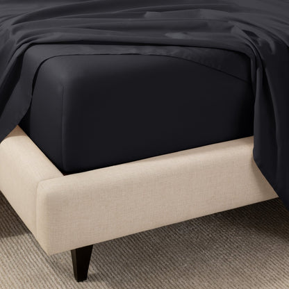 A close-up of the corner of a bed with a fitted sheet and matching flat sheet.