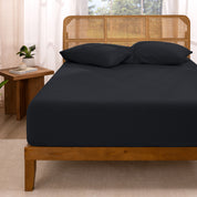 Bed with fitted sheet and pillows in a room with curtains and a plant.