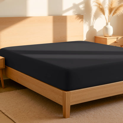 Fitted sheet on a bed in a bedroom setting with a lamp and plant.