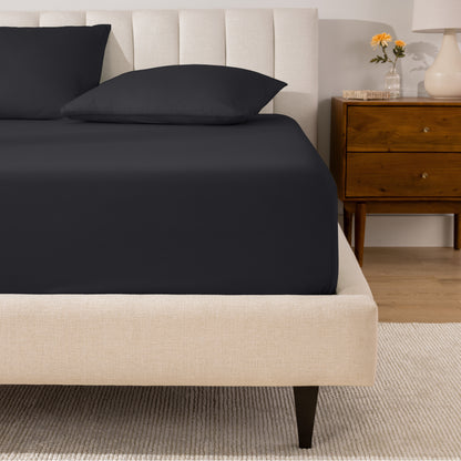 A percale fitted sheet and pillowcases on a bed in a bedroom with a wooden nightstand.