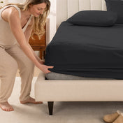 Woman in pajamas adjusting bed sheets on a bed.