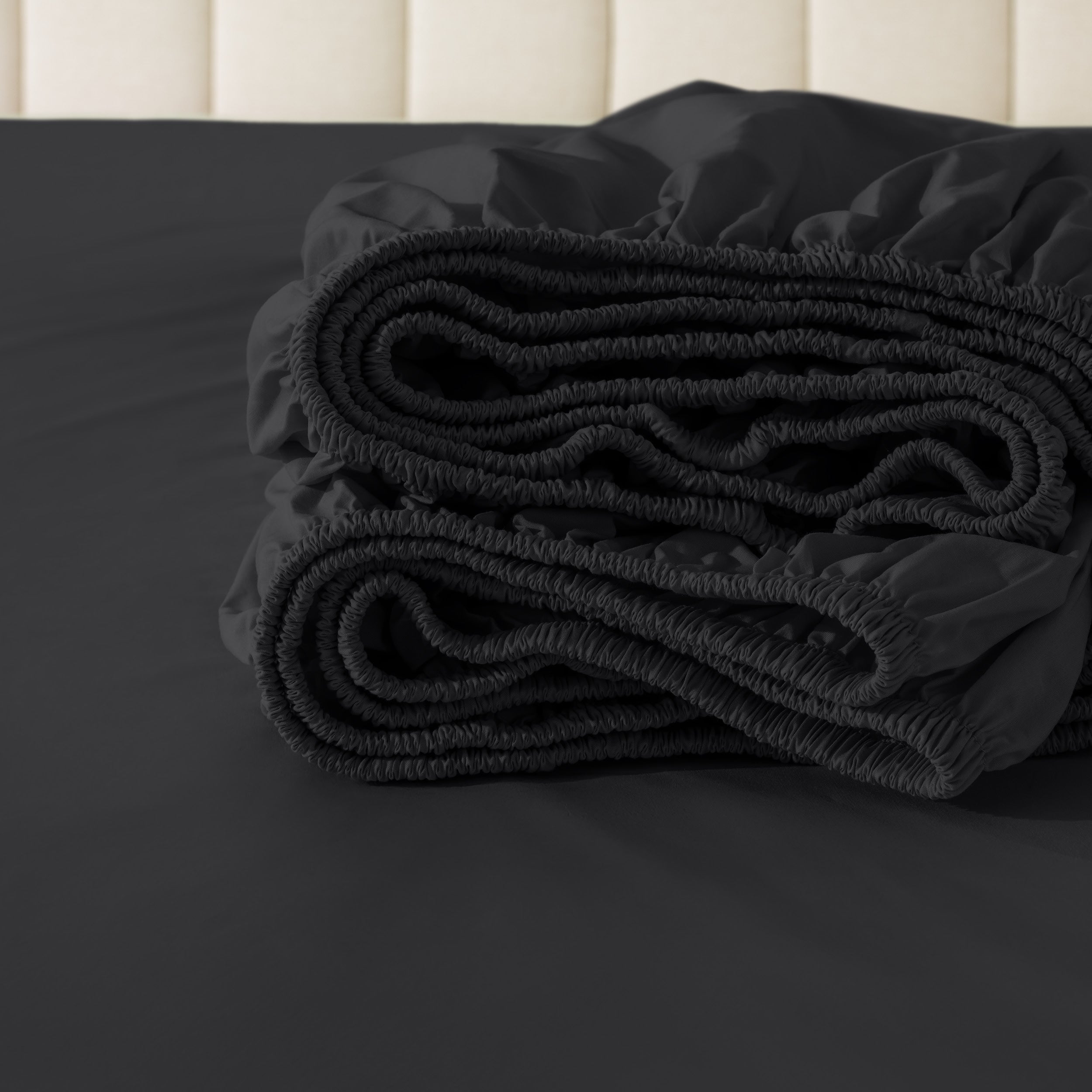 Folded fitted sheet on a bed with a neutral background