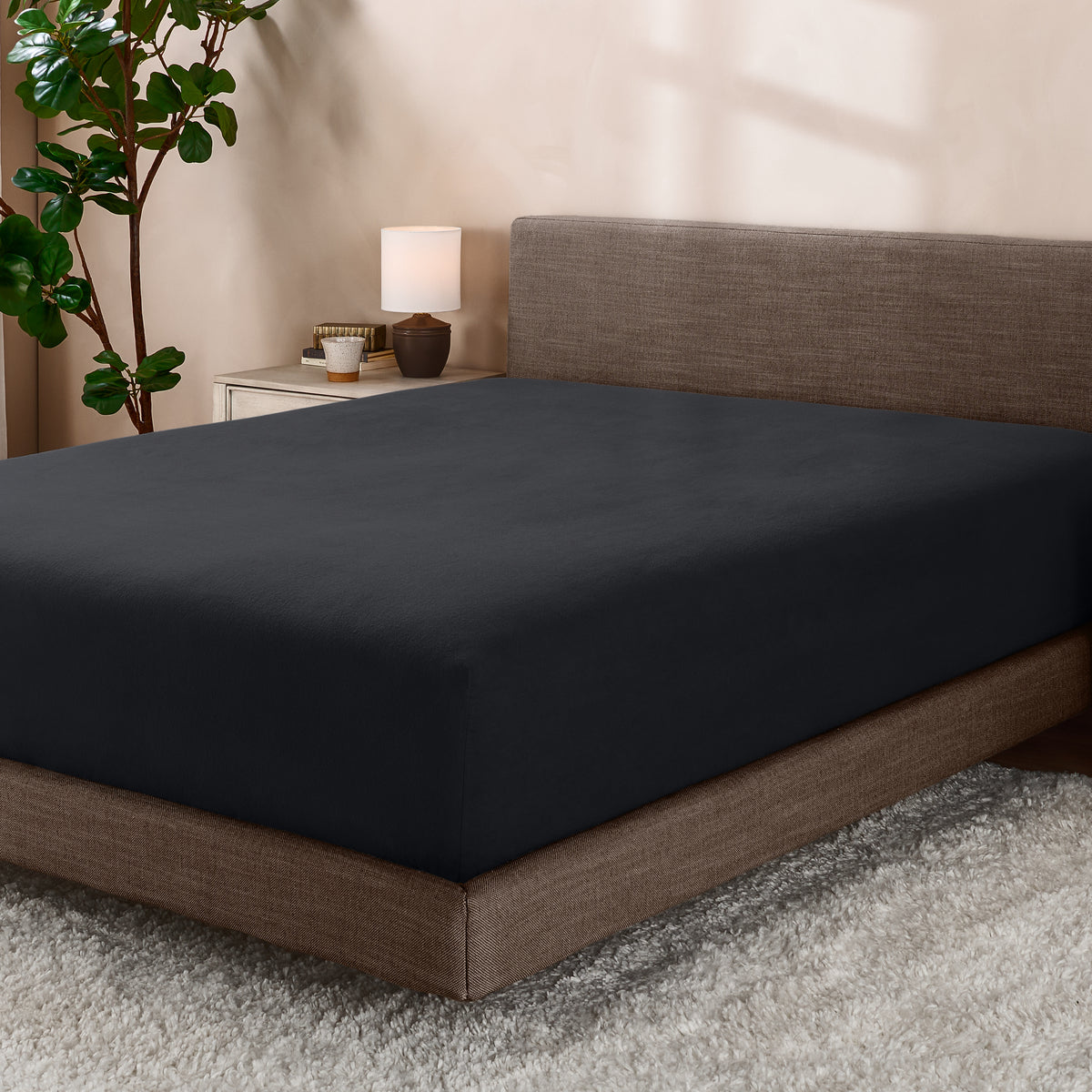 Bed with fitted sheet in a room with a lamp and plant.