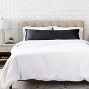 Black satin pillow on a bed with white bedding and a wooden headboard.