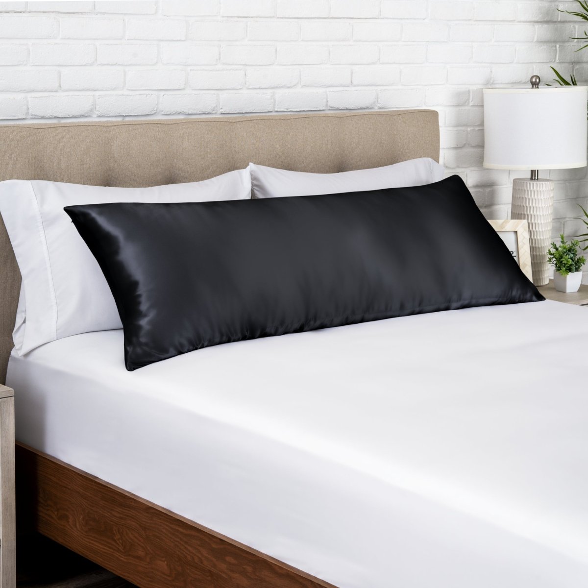 Black satin pillow on a bed with white bedding and a wooden headboard.