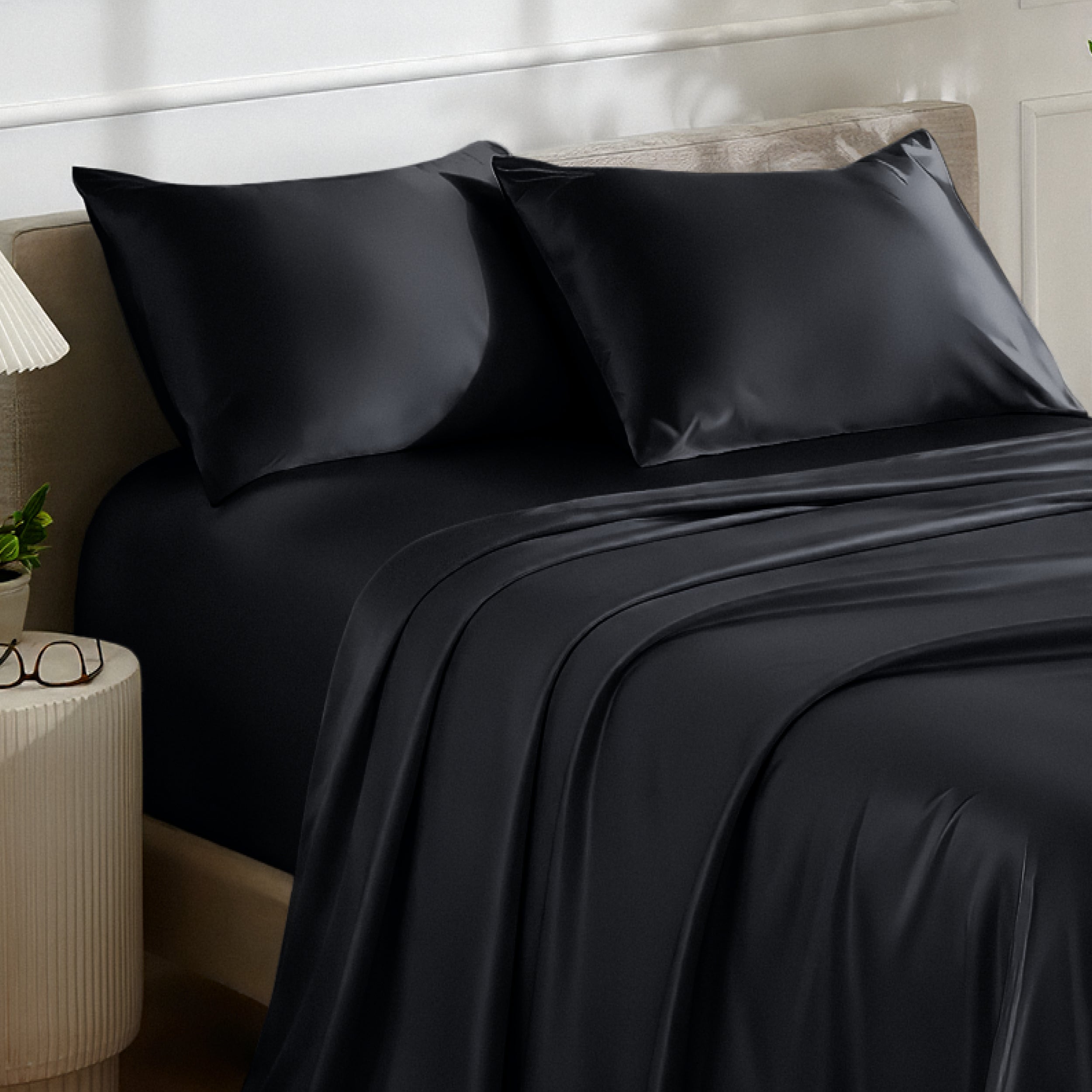 Satin bedding set on a bed with a nightstand and lamp in the background.