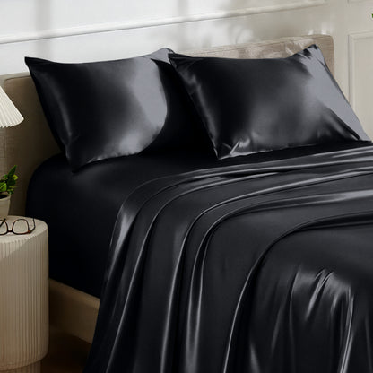 Satin bedding set on a bed with a nightstand and lamp in the background.