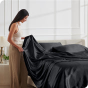 A woman is putting satin sheets on a bed