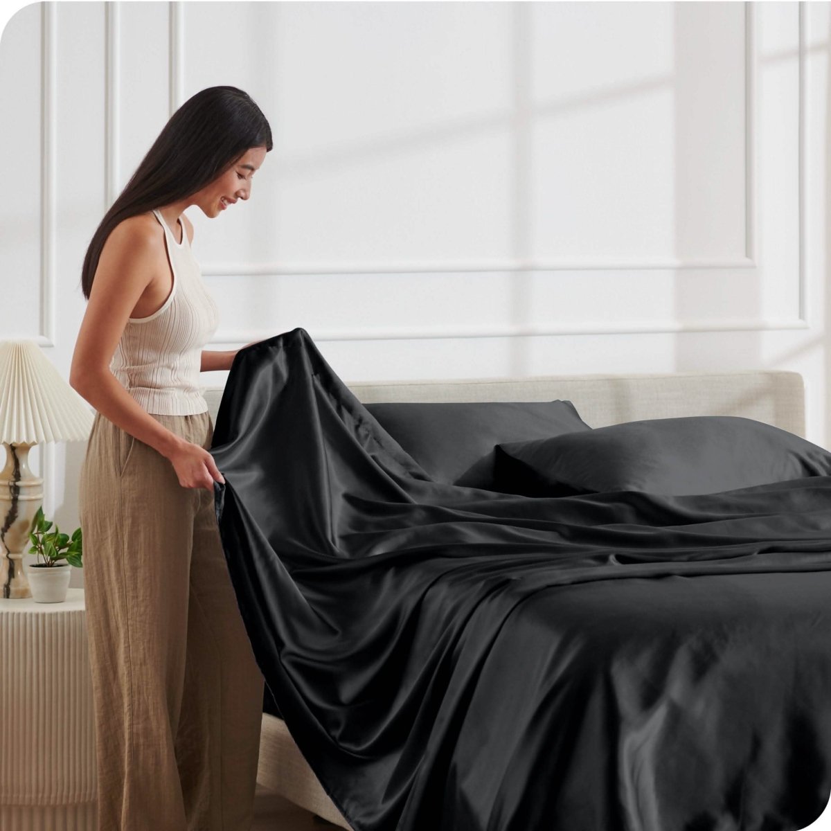 A woman is putting satin sheets on a bed