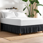 Bed with bed skirt, white bedding, and a plant in a room.