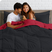 A couple sitting in a bed made with a reversible comforter and sheet set