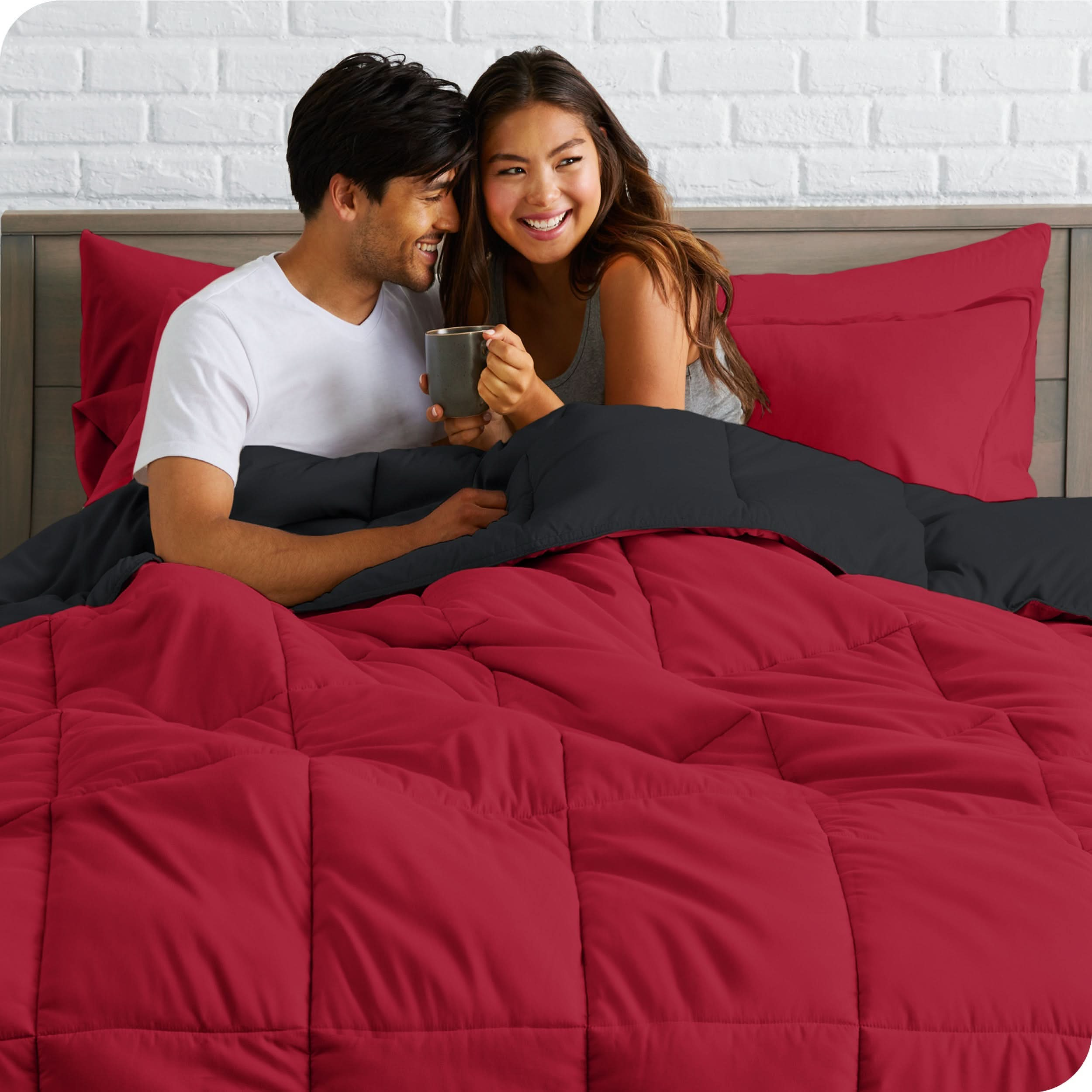 A couple sitting in a bed made with a reversible comforter and sheet set