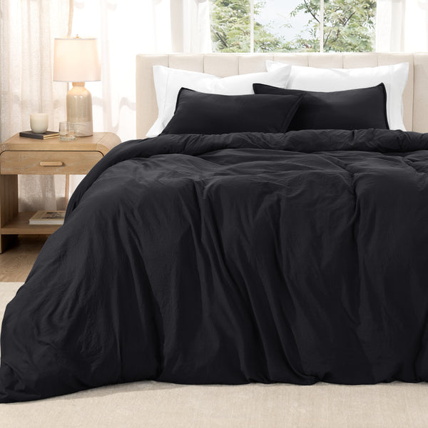 Washed duvet set on a bed in a bright bedroom with a lamp and window.