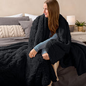 Fluffy blanket draped over a woman sitting on the end of a bed