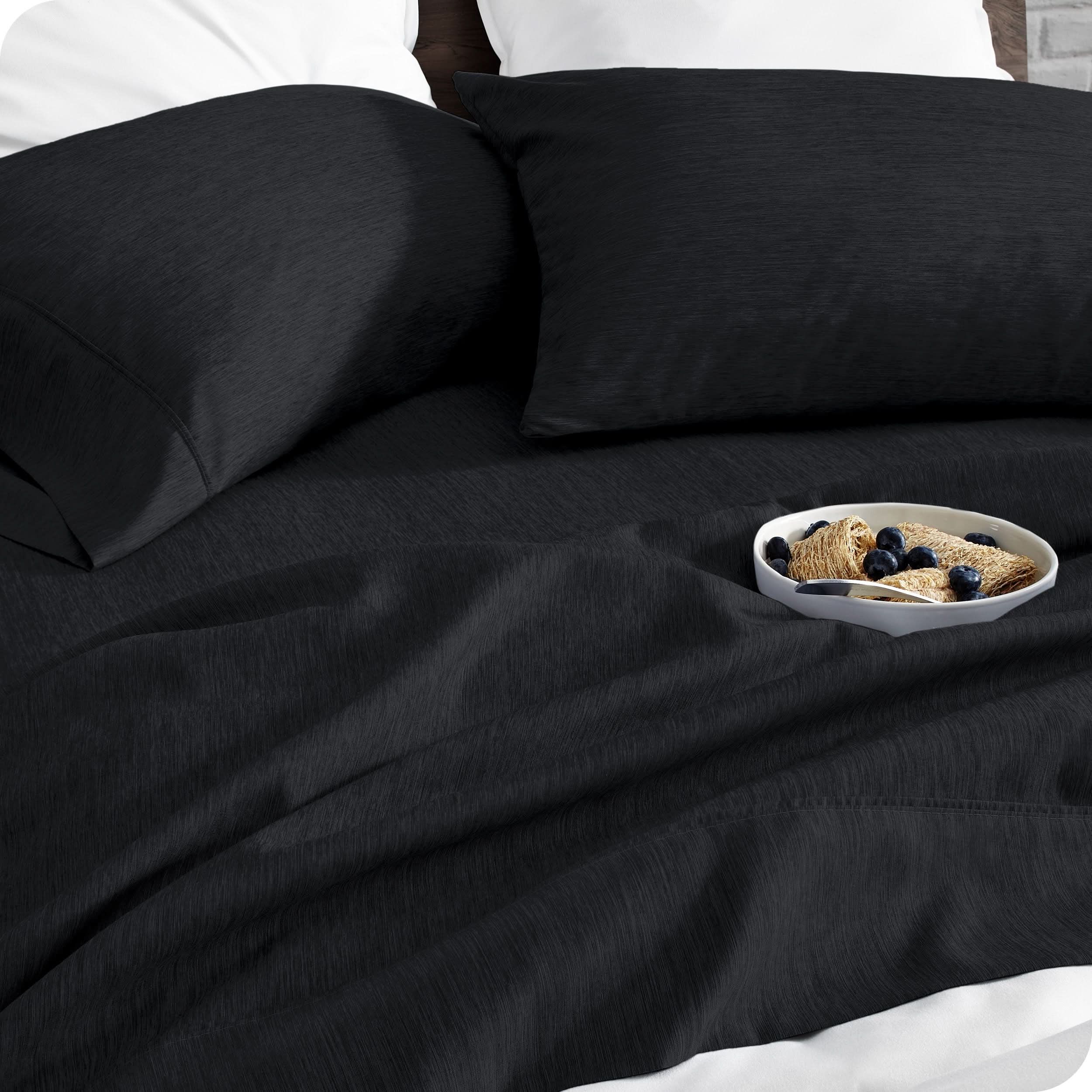 A bed made with sheets. A cereal bowl is on the sheets.