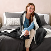 A woman sitting on a bed with a Sherpa blanket around her