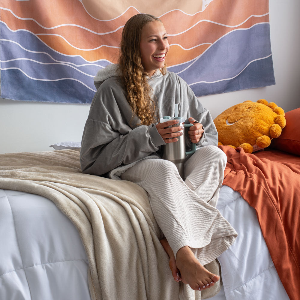 Woman sitting on her bed in a dorm room wearing a wearable blanket