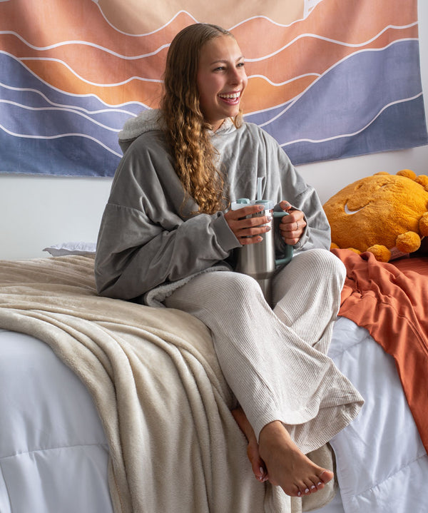 Woman sitting on her bed in a dorm room wearing a wearable blanket