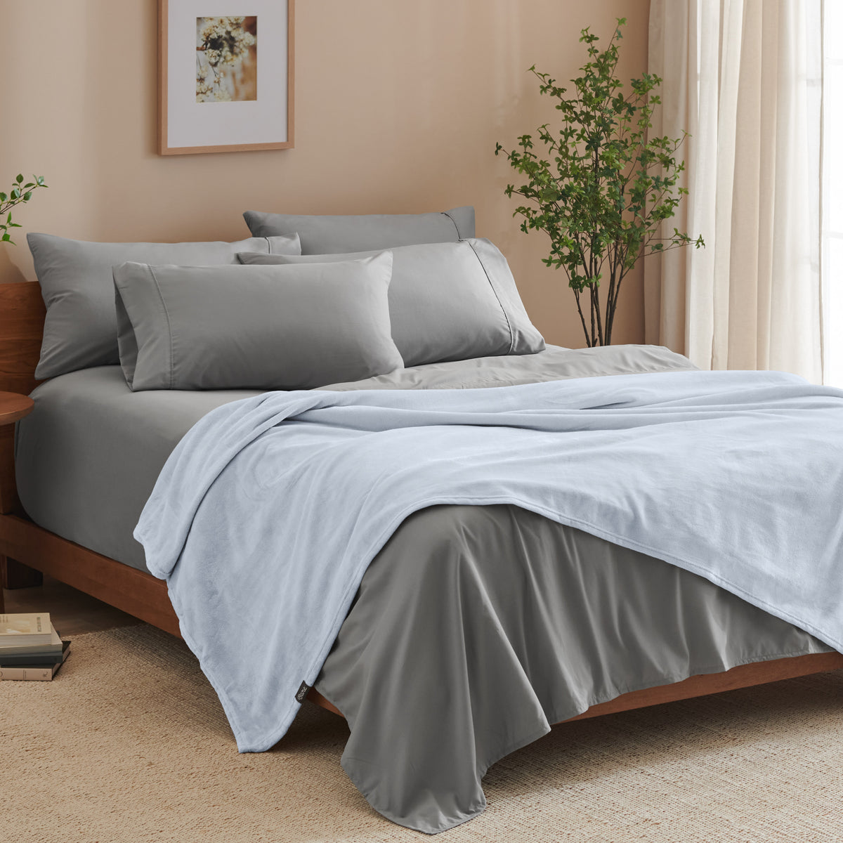 A bed made with grey sheets and a microplush blanket