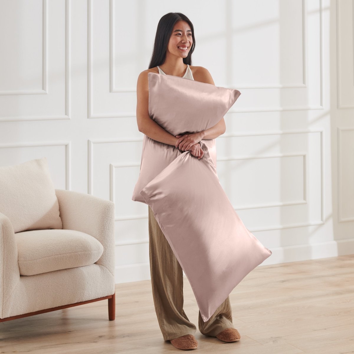 Woman holding 2 pillows with satin pillowcases on them