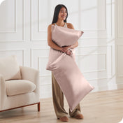 A woman has 2 pillows in her hands and they have satin pillowcases on them