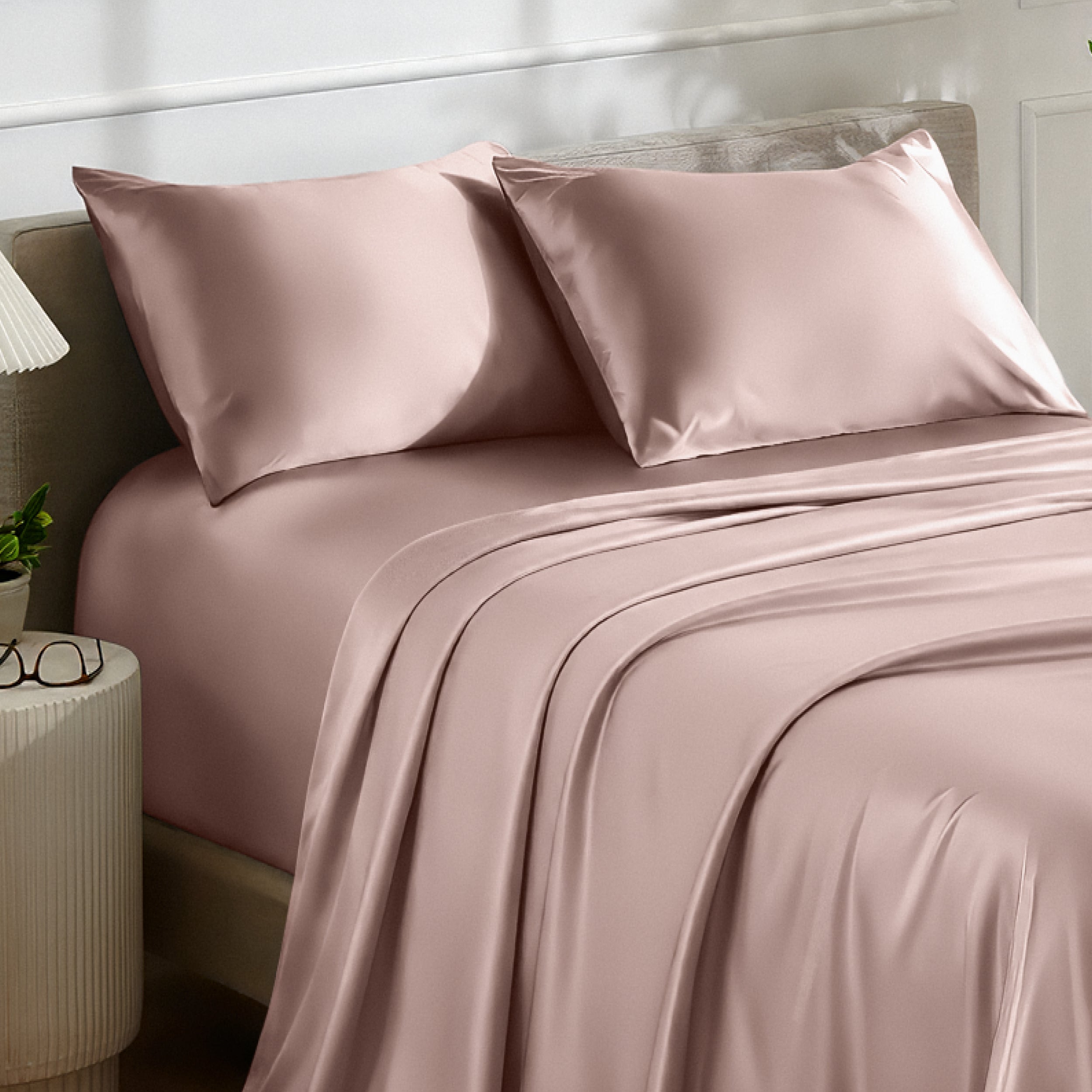 Satin bedding set on a bed with a nightstand and lamp in the background.