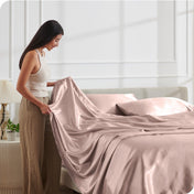 A woman is putting satin sheets on a bed
