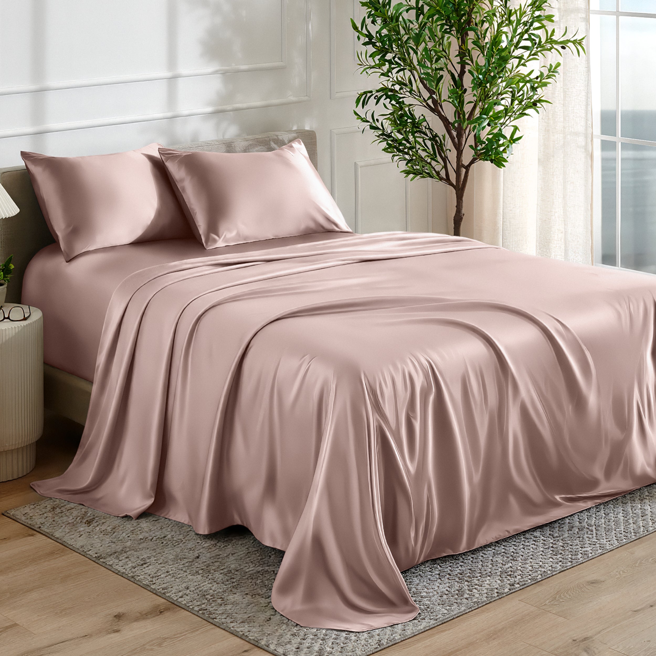Satin sheet set on a bed in a bedroom with a plant and window in the background.