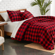 Red and black checkered bedding set on a bed in a bedroom with a plant and side table.