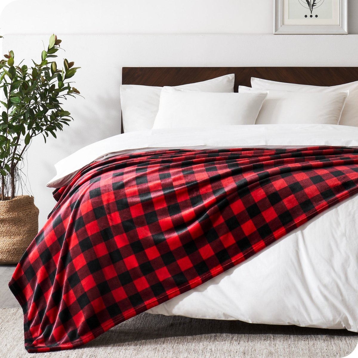 Red and black checkered blanket draped over a bed with white pillows and a plant in the corner.