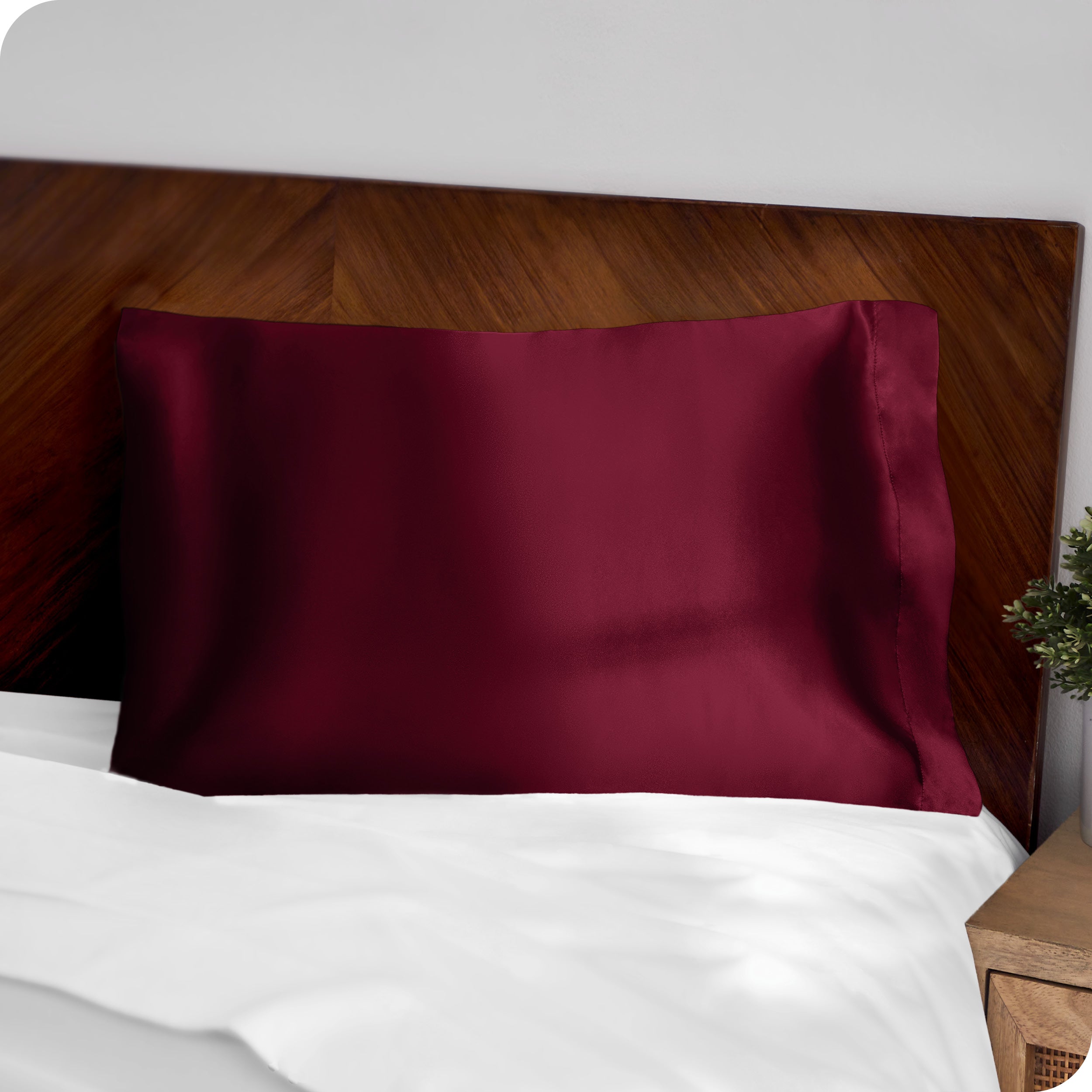 A red silk pillowcase on a pillow resting on a headboard