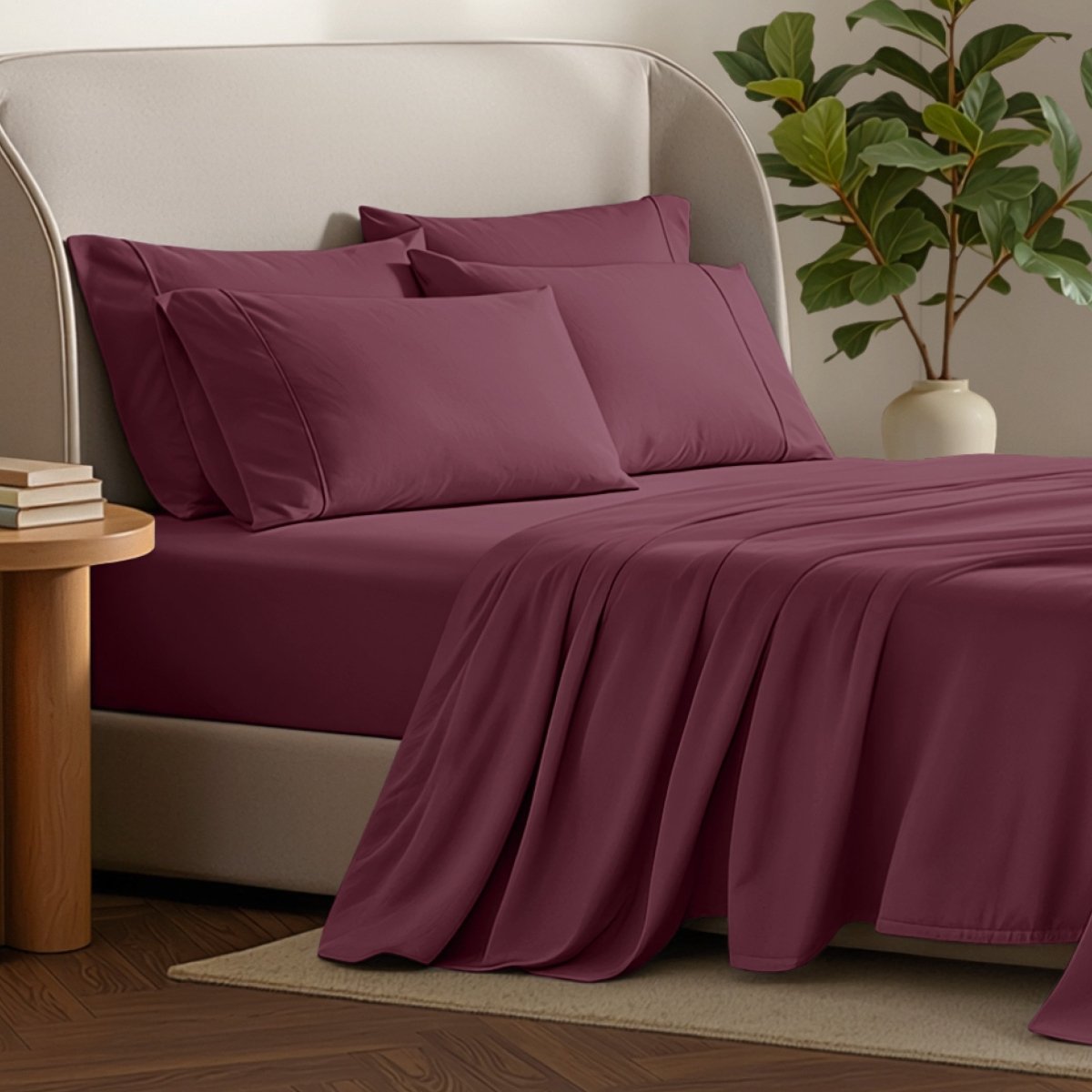 Bed sheets and pillows on a bed with a plant and side table in the background.