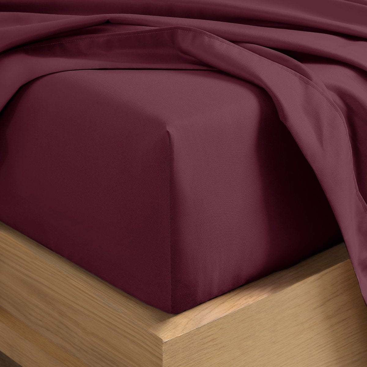A close-up of a fitted sheet covering the corner of a bed frame, with matching top sheet draped over it.