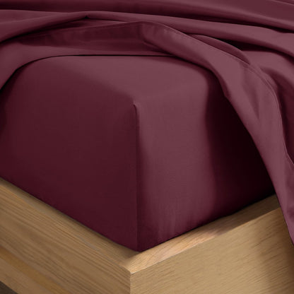 A close-up of a fitted sheet covering the corner of a bed frame, with matching top sheet draped over it.