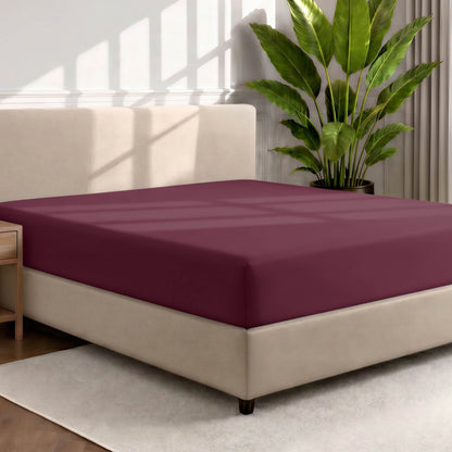 Bed with a fitted sheet in a room with a large plant and rug