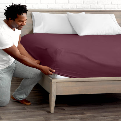 Man adjusting fitted sheet on a bed with white pillows.