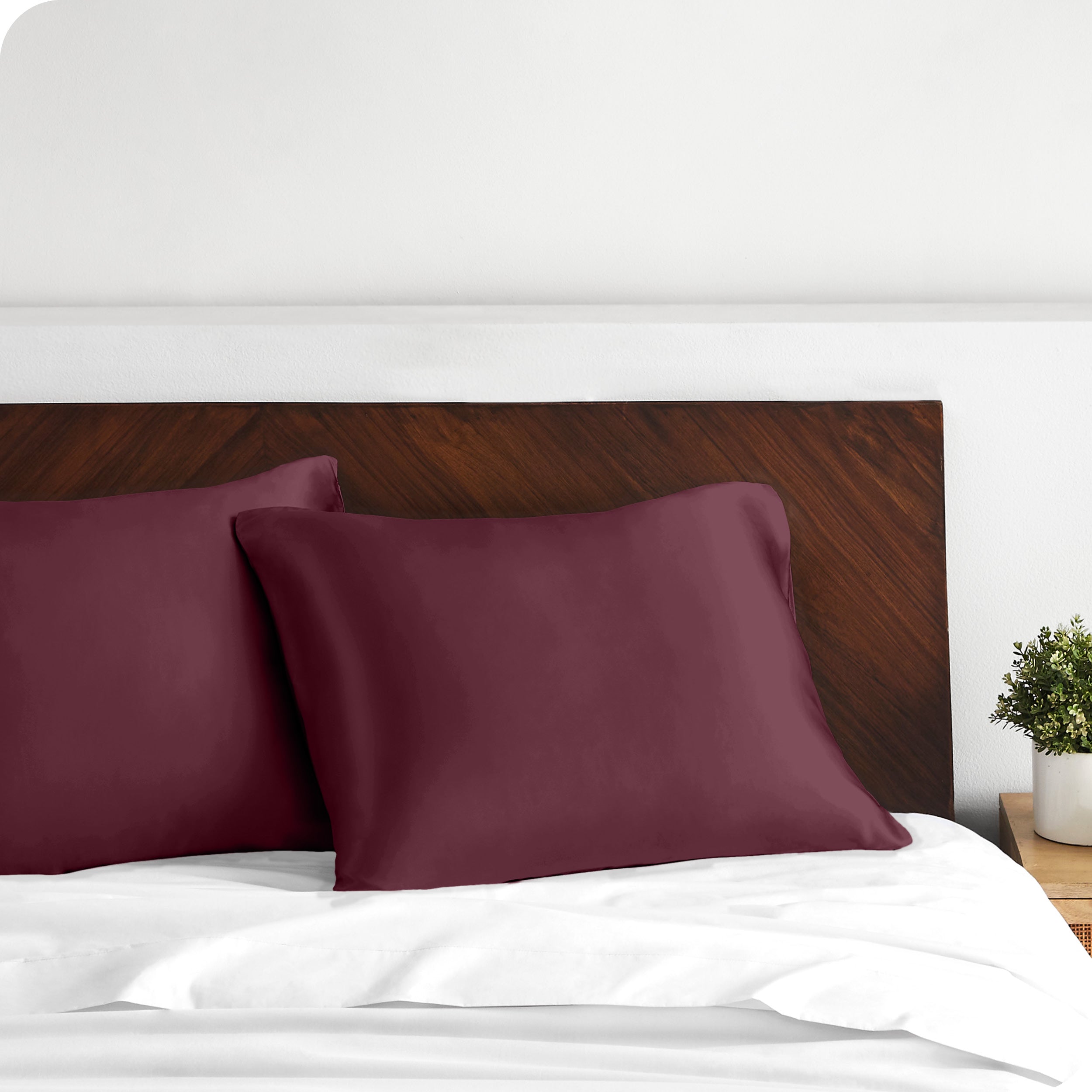 Two satin pillowcases on pillows against a wooden headboard