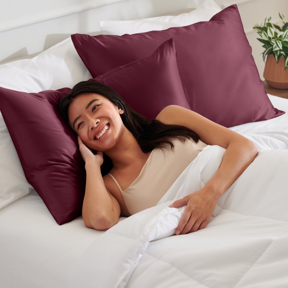 Woman lying on a bed with satin pillows and white bedding