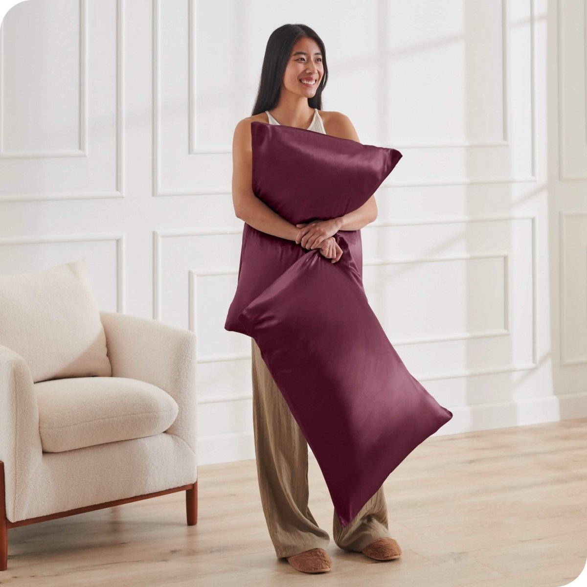 A woman has 2 pillows in her hands and they have satin pillowcases on them