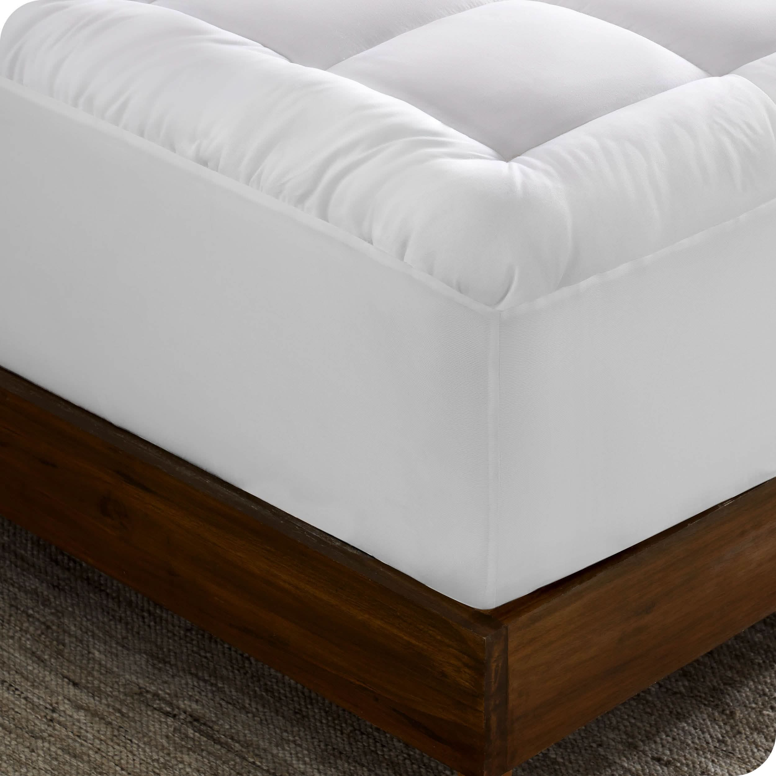 A corner of a mattress on a wood frame. A mattress pad is covering the mattress.