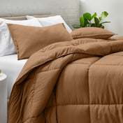 Comforter and pillow shams on a bed with a white brick wall and plant in the background