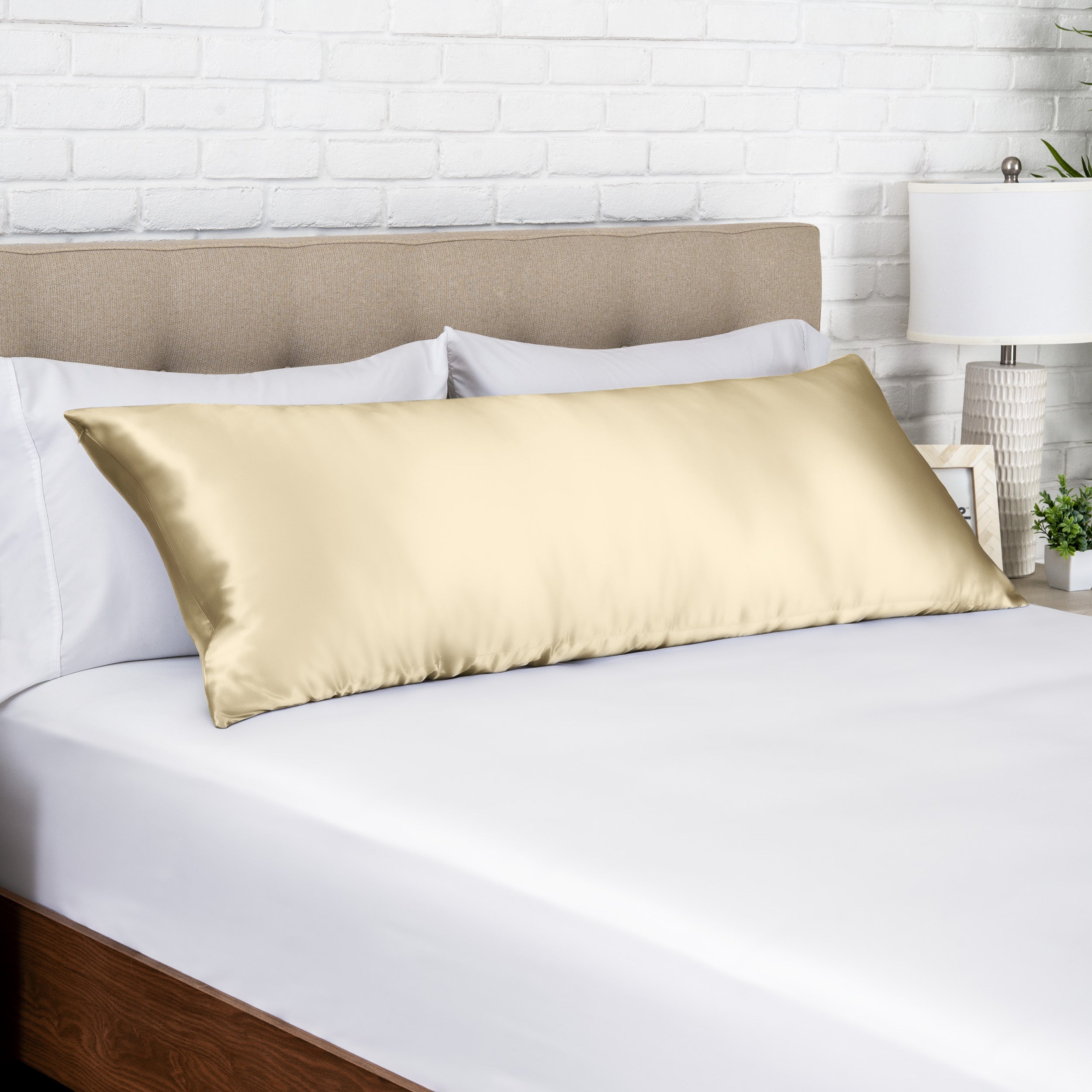 Champagne silk pillow on a bed with white bedding and a beige headboard.