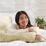 Woman lying on a bed with a body pillow, smiling.