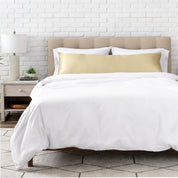 Bed with white bedding and satin pillowcase against a white brick wall.