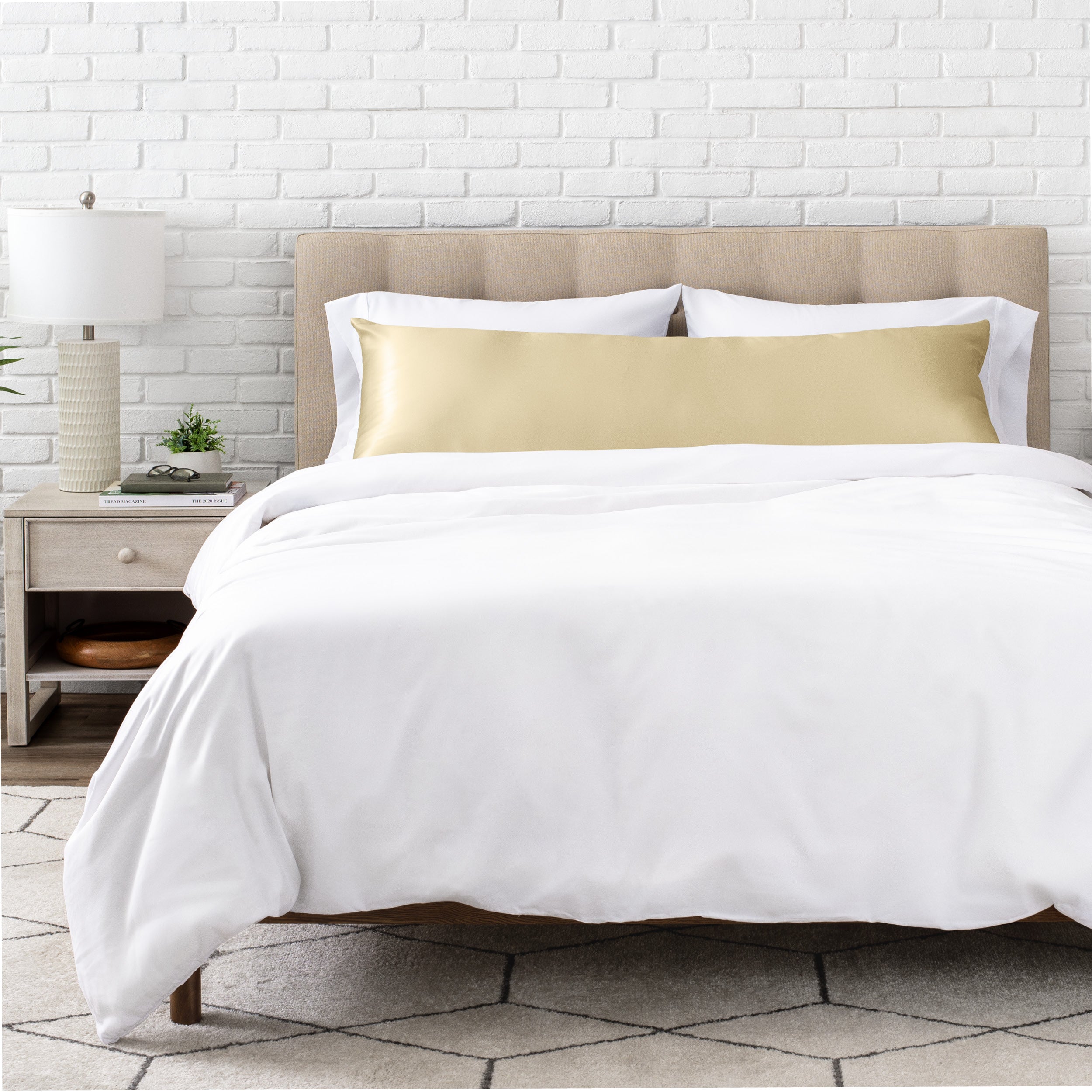 White bedding set with body pillow covered with a silk pillowcase on a bed in a bedroom setting.