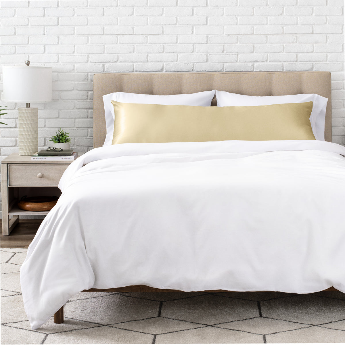 White bedding set with body pillow covered with a silk pillowcase on a bed in a bedroom setting.
