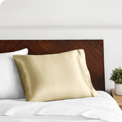 A champagne silk pillowcase on a pillow resting on a headboard