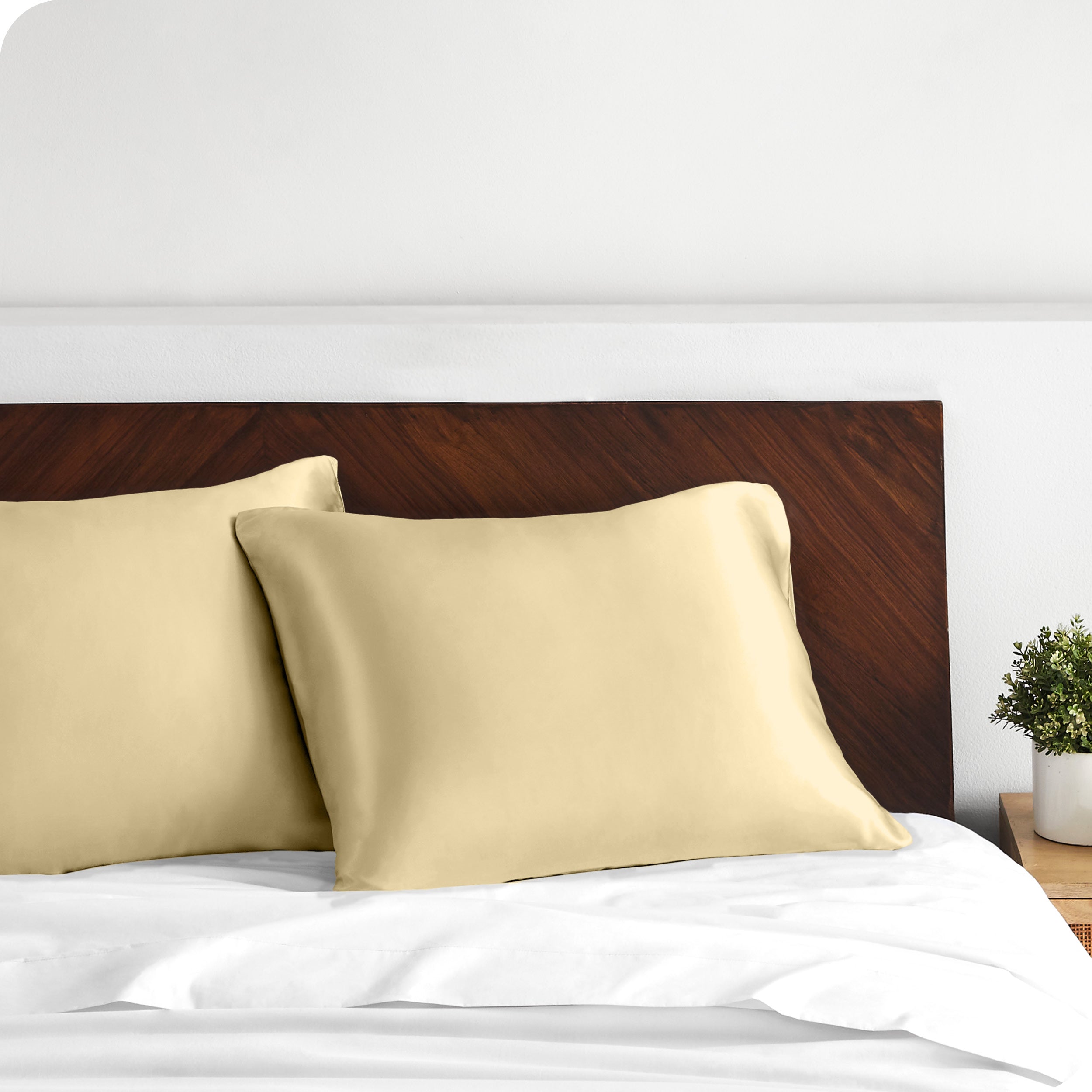 Two satin pillowcases on pillows against a wooden headboard