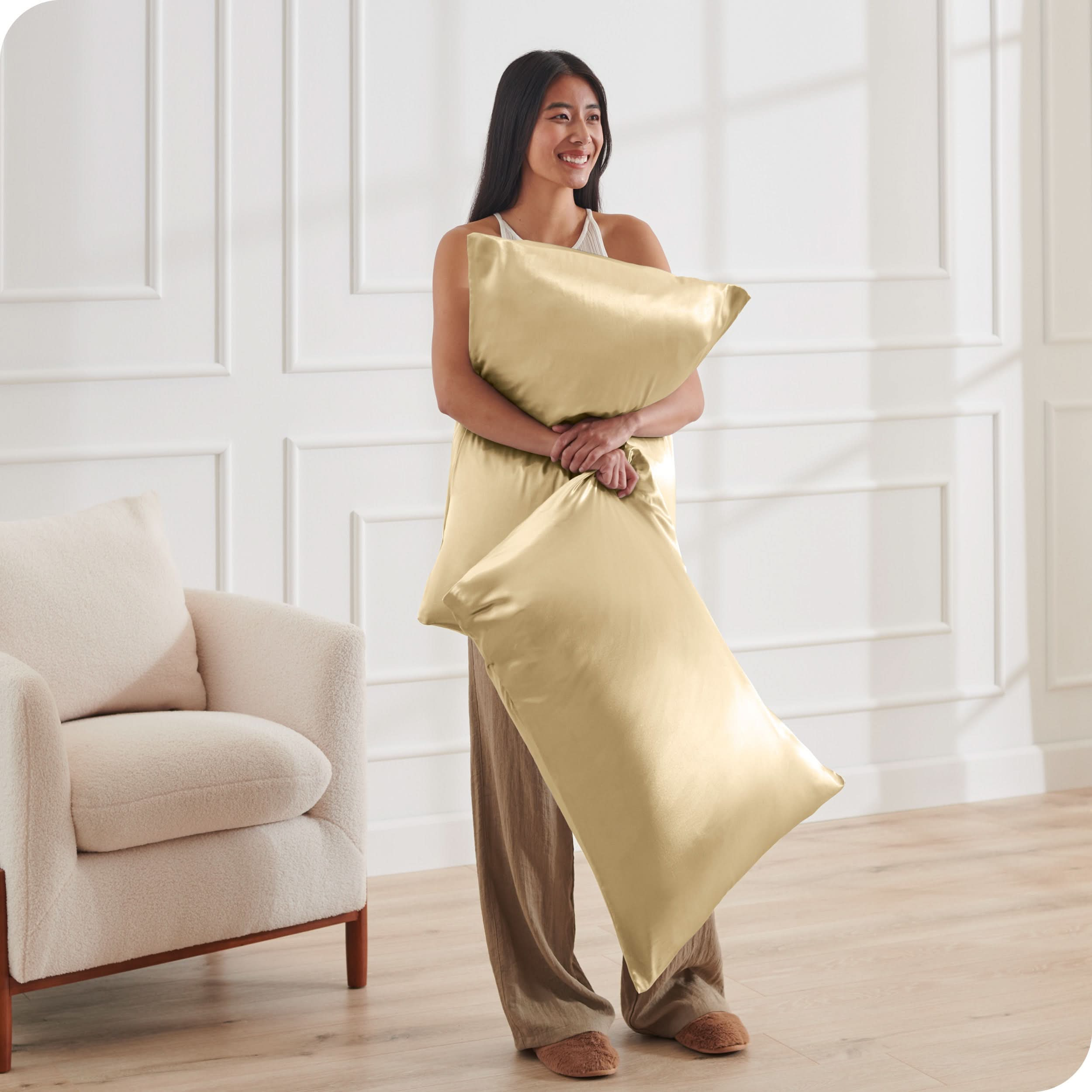 A woman has 2 pillows in her hands and they have satin pillowcases on them