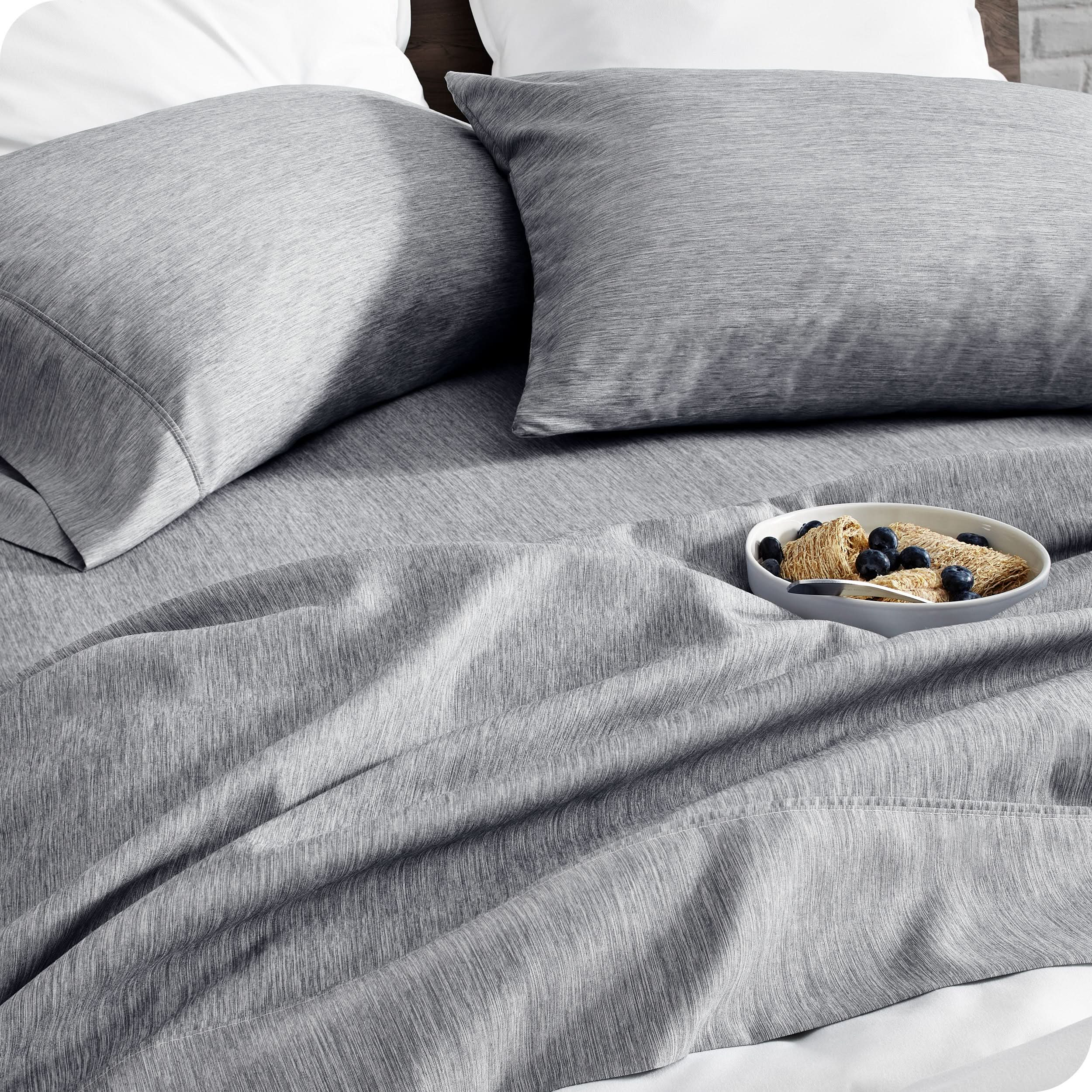 A bed made with sheets. A cereal bowl is on the sheets.